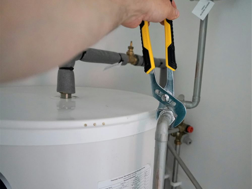 Plumber tightening a fitting on top of a water heater with pliers